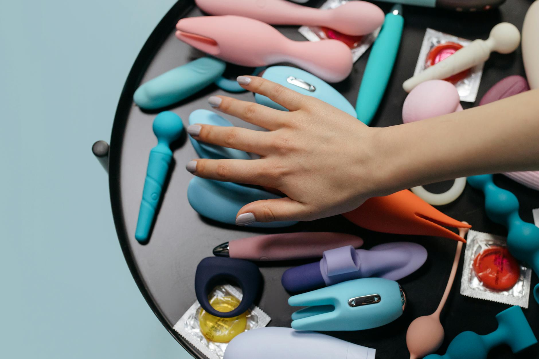 Eine Hand greift über eine Auswahl an bunten Vibratoren auf einem Tisch.