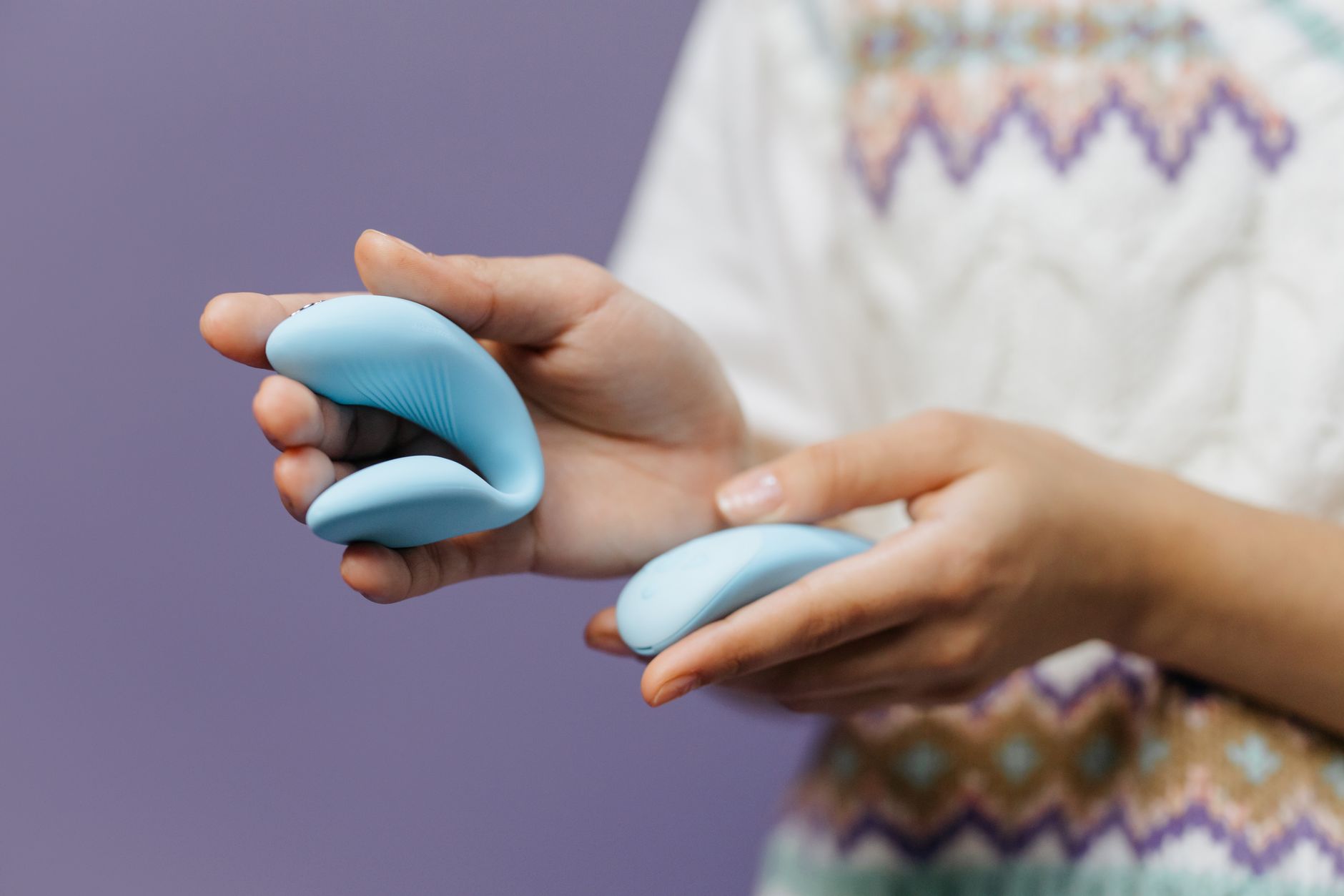 Nahaufnahme: Hände halten einen schlanken blauen Vibrator gegen einen lila Hintergrund
