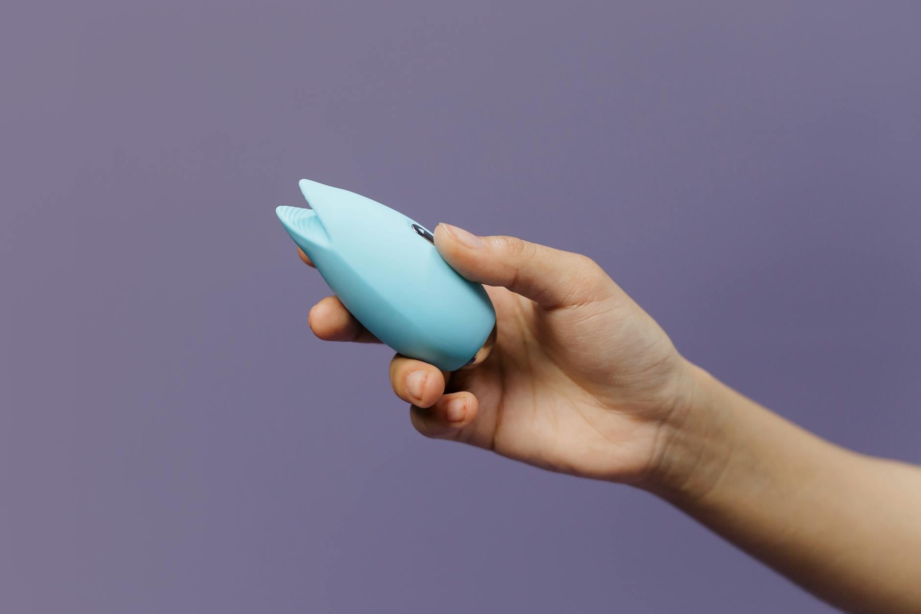 Zwei Hände halten rosa und blaue Silikonvibratoren gegen einen pastellfarbenen Hintergrund.