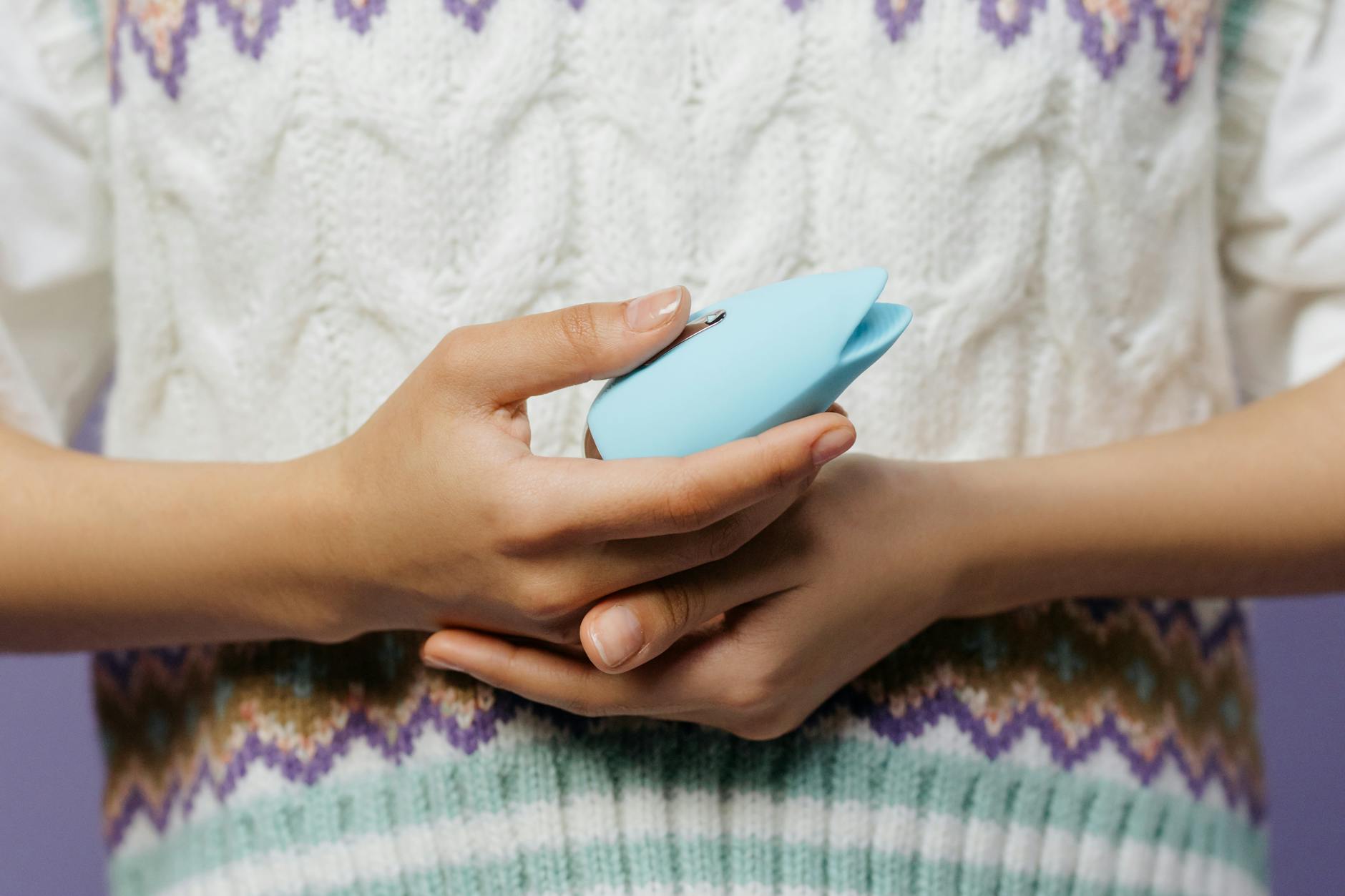 Nahaufnahme: Hände halten einen blauen Vibrator gegen einen gestrickten Pullover