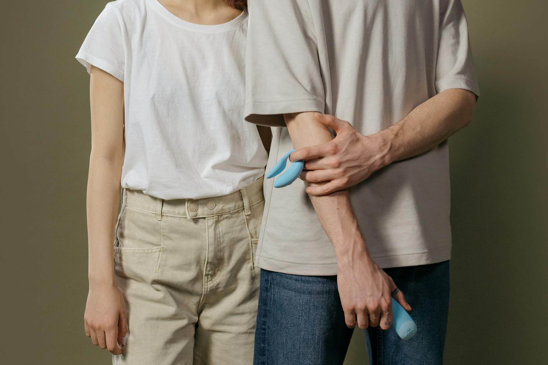 Ein Paar steht zusammen, beide halten einen blauen Vibrator, Symbol für moderne Partnerschafts-Intimität.