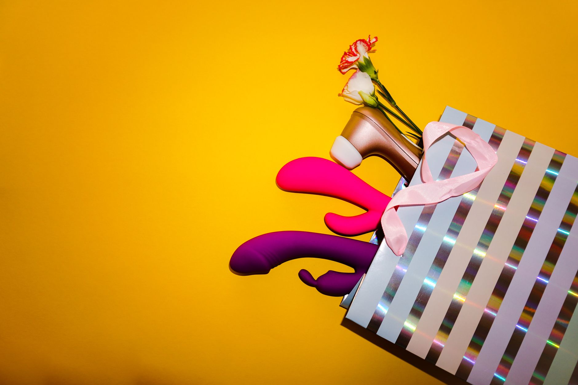 Farbenfrohe Zitronenvibratoren mit Blüten in einer holografischen Geschenktasche vor gelbem Hintergrund