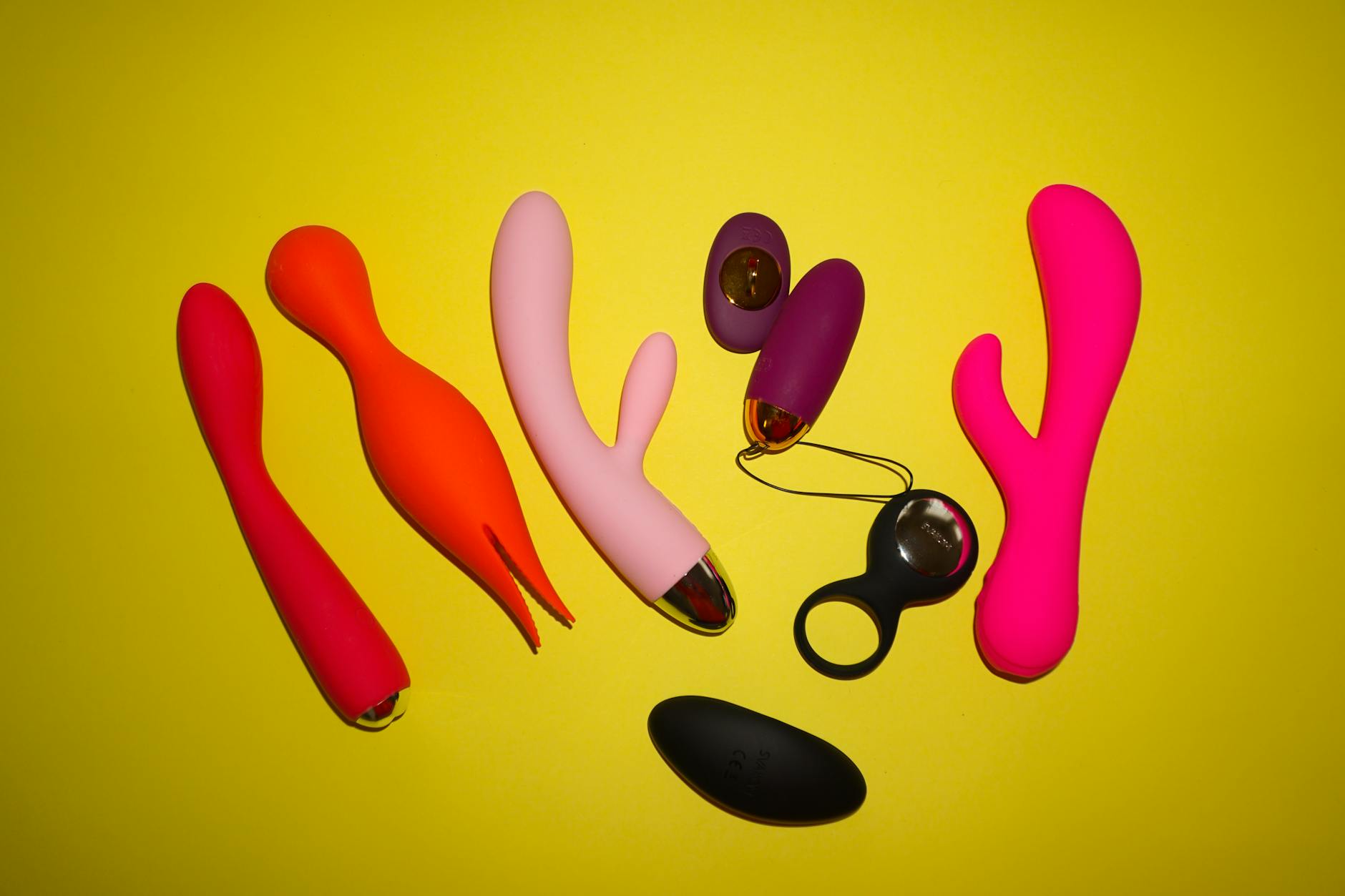 Frau hält zwei bunte Vibratoren in nachdenklicher Pose
